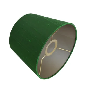 Close-up van een conische lampenkap van donkergroene wilde zijde, schuin op zijn zijkant liggend. De binnenzijde is goudkleurig met een metalen bevestigingsring en drie spijlen. De geweven textuur van de zijde is duidelijk zichtbaar over het gehele oppervlak.