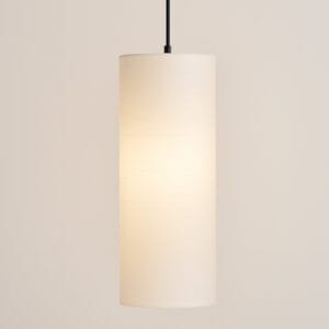 Witte smalle lampenkap hangend aan zwart snoer in een neutraal interieur. Op de achtergrond een muur in een zachte beige tint