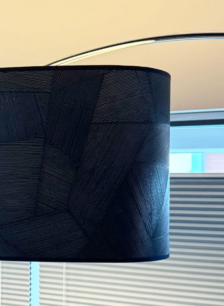 Dezelfde blauwe lampenkap gefotografeerd in een warmere lichtinval, waardoor het donkere contrast en de grafische vlakken van het Arte-behang extra sterk naar voren komen. Een speelse, elegante lamp voor een stijlvol interieur.